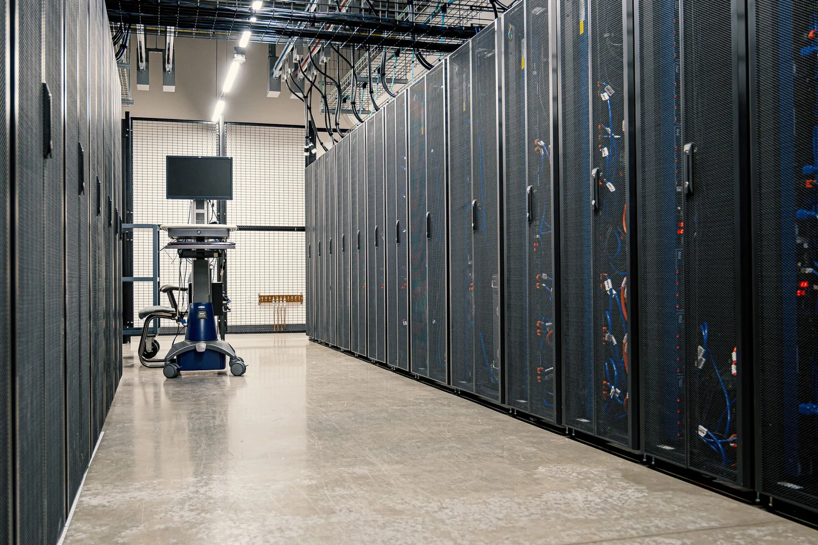 Long aisle of server racks, network cabling, and overhead cable trays inside a data center